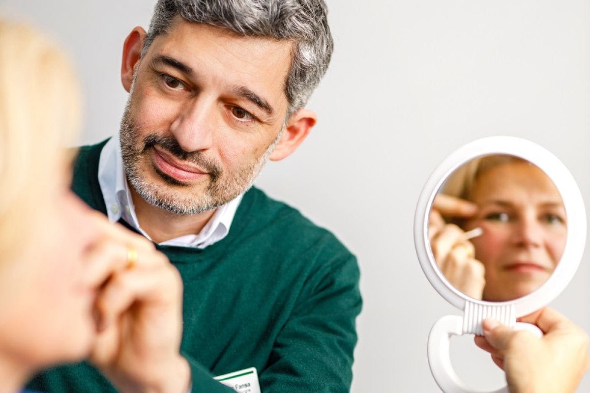 Middle-aged man looking at himself in a hand mirror and using tweezers.