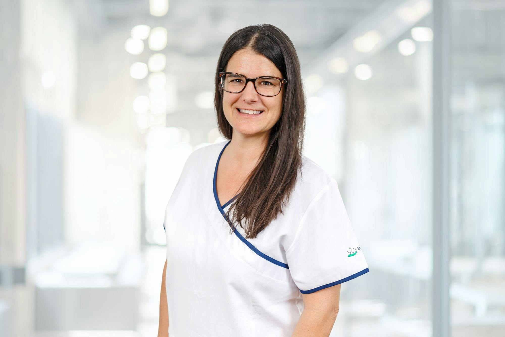 Lächelnde Frau in medizinischer Berufskleidung mit Brille.