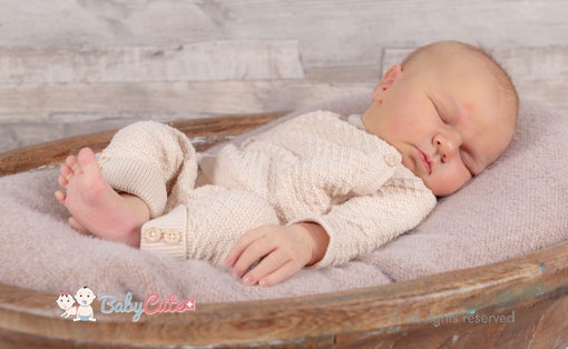 Schlafendes Baby in beiger Strickkleidung auf einer lila Decke.