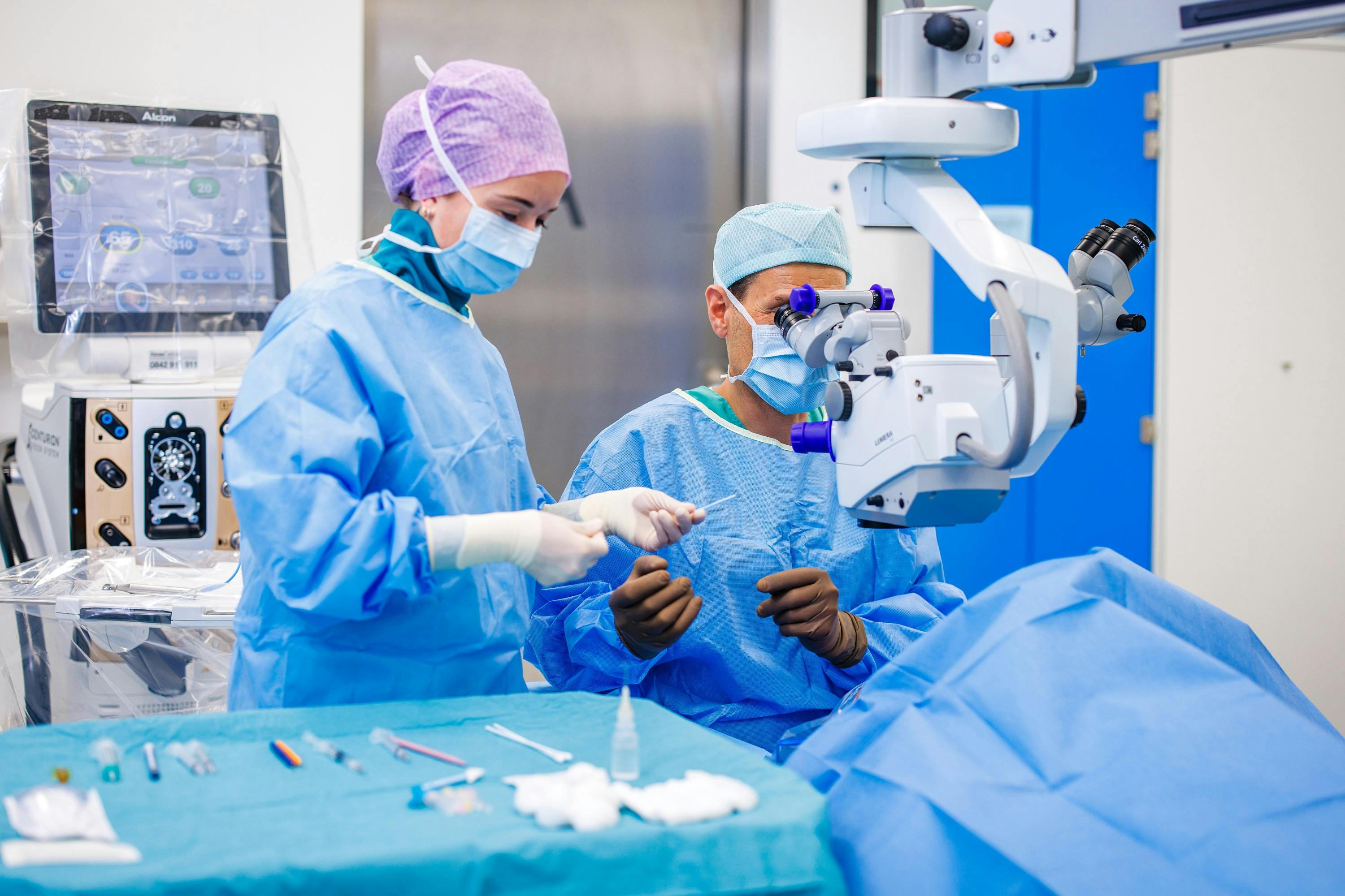 Chirurgen in blauen OP-Kleidung bei der Arbeit mit Mikroskop und Instrumenten.
