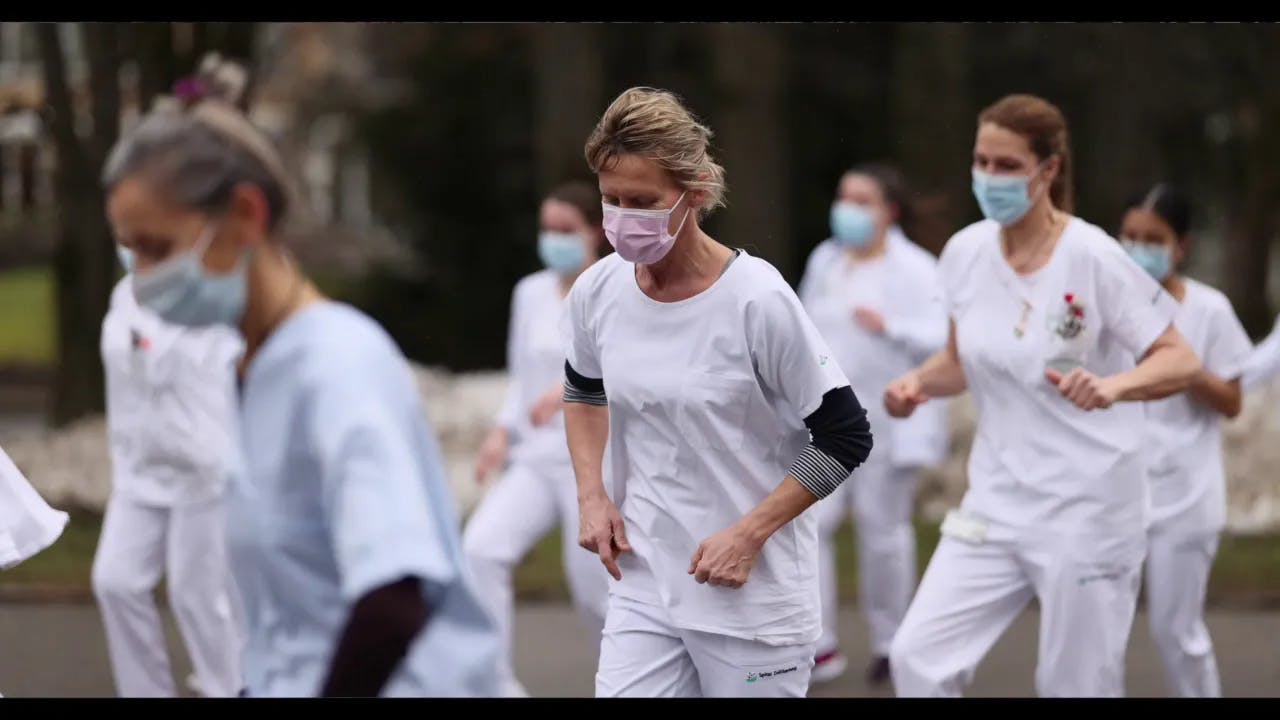Hospital staff in white scrubs and face masks during an outdoor exercise.